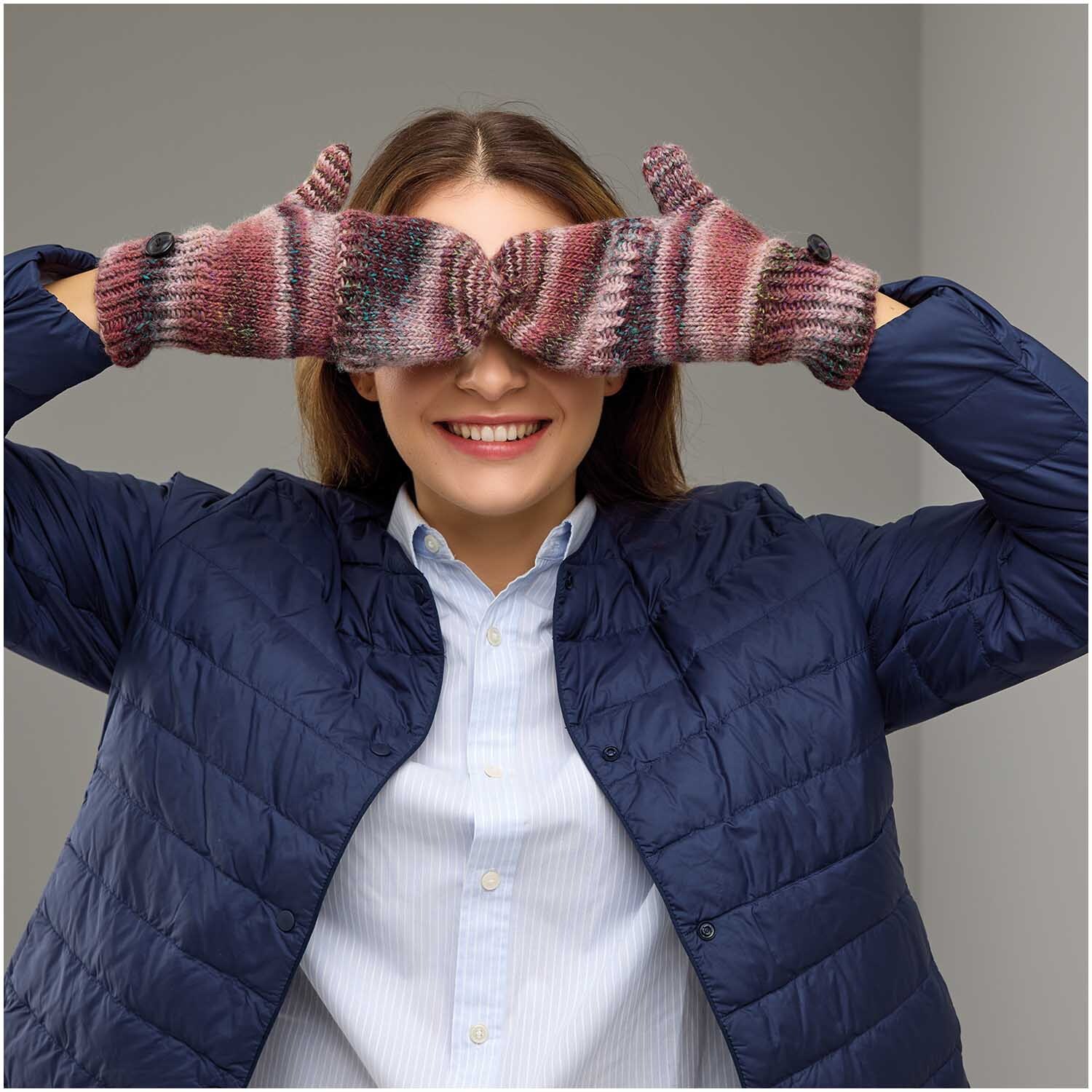 Strickset Fäustlinge Modell 27: Frau trägt bunte Fäustlinge und blaue Jacke, lächelnd mit Händen vor den Augen.