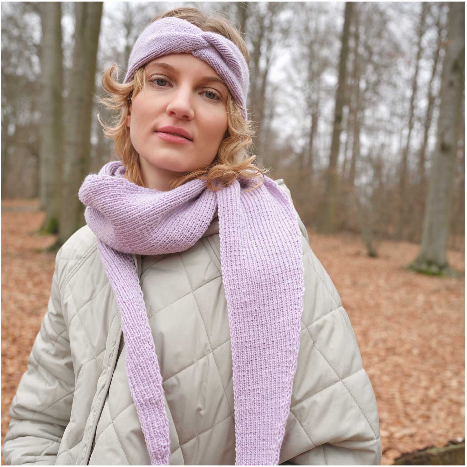 Strickset Stirnband Modell 15: Frau im Wald mit lila Stirnband und Schal, beige Jacke.