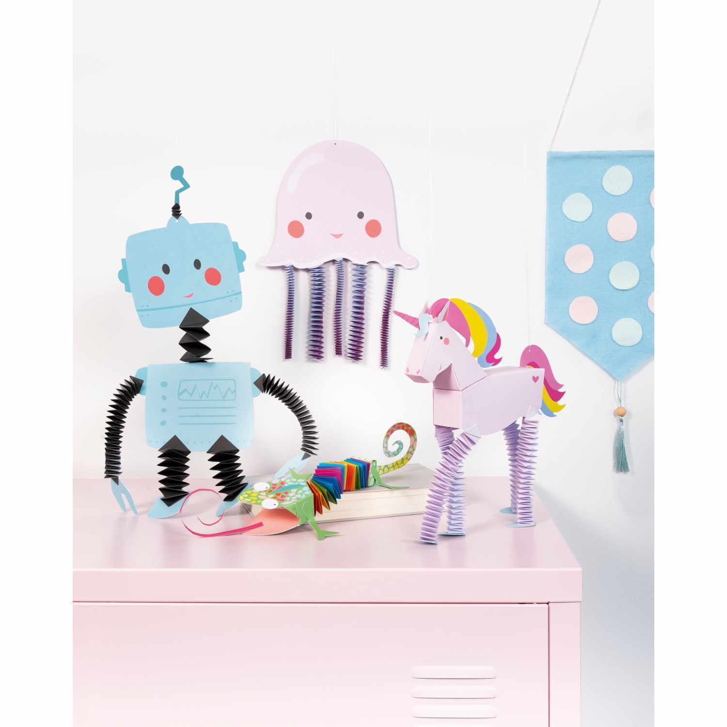 Hexentreppen Bastelset Charming Friends für 10 Figuren zeigt bunte Papierfiguren wie Roboter, Qualle und Einhorn auf einem Tisch.