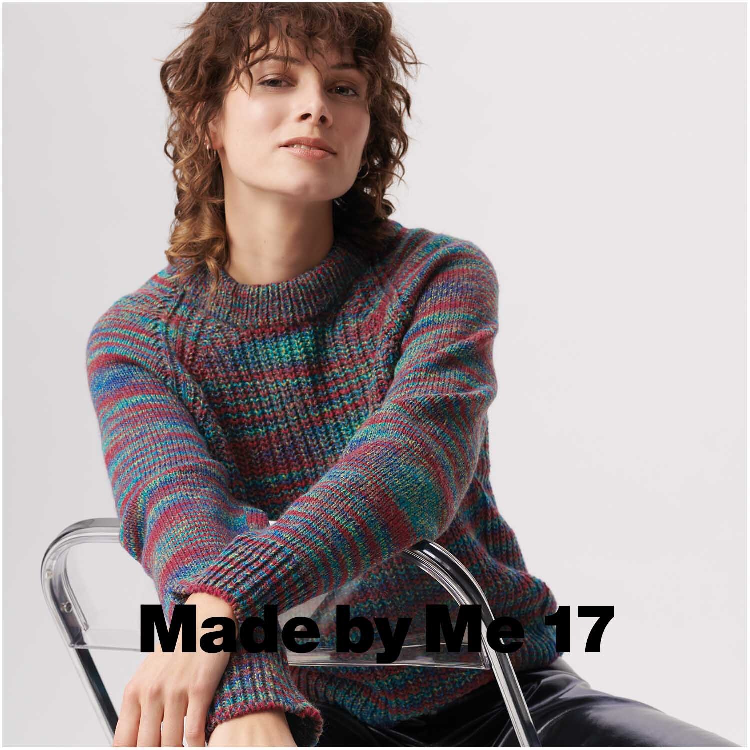 Creative Colour Shift dk: Frau in gestricktem Pullover mit Regenbogenmuster von Rico Design, sitzt auf einem Stuhl.