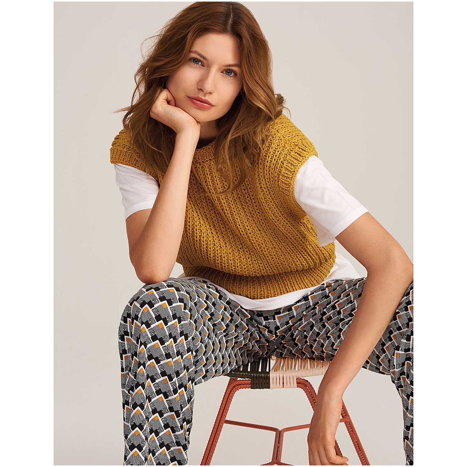 Fashion Linen Swell aran: Frau trägt senfgelbes Strickoberteil von Rico Design, kombiniert mit gemusterten Hosen.