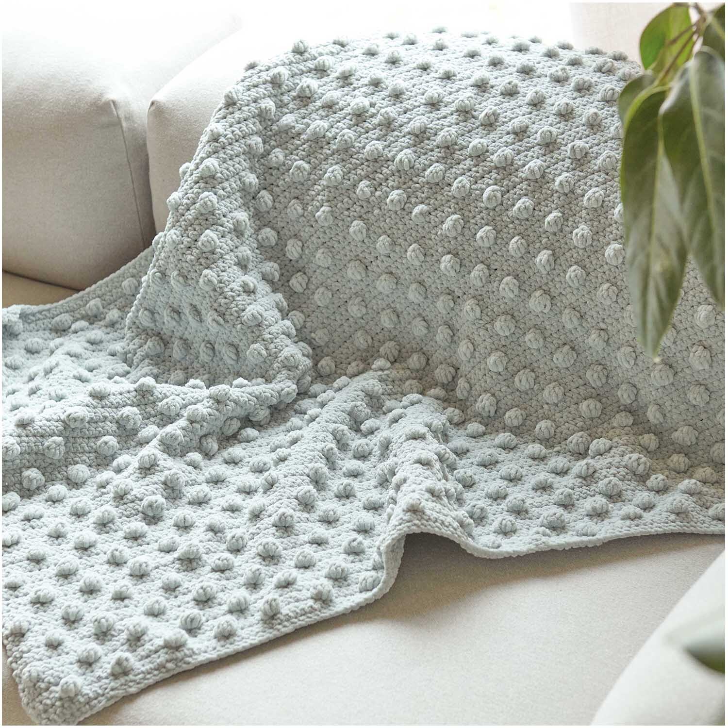 Creative Chenillove Decke in weichem Aqua auf einem Sofa, ideal für gemütliche Stunden. Hochwertige Qualität von Rico Design.