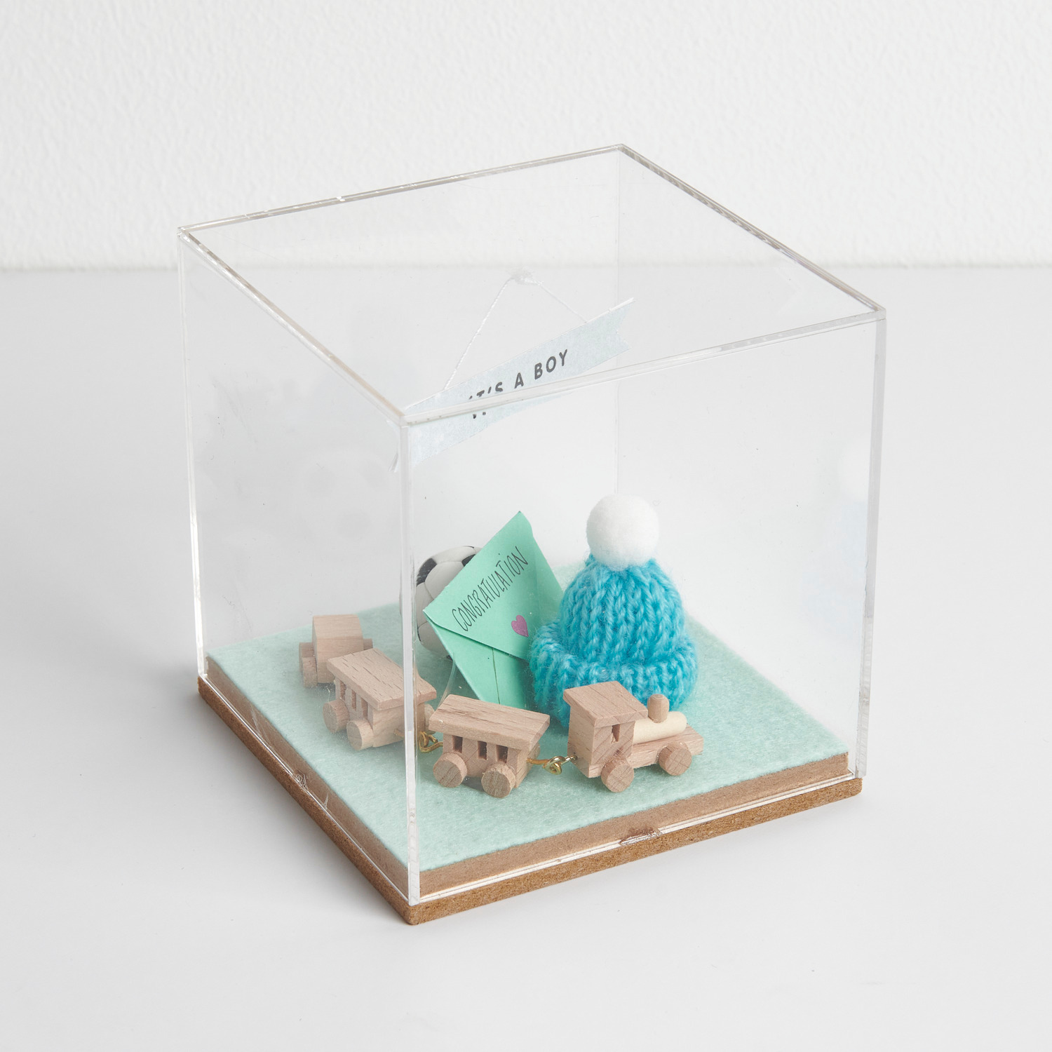 Figurico Dekohaube Würfel mit Holzspielzeug und blauem Strickmütze auf grünem Filzboden.