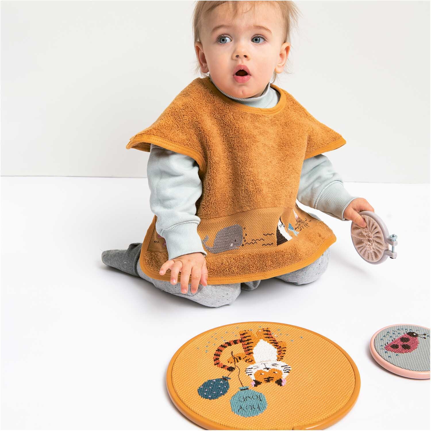 Stickring aus Kunststoff senf 22,8cm von Rico Design. Kind spielt mit gelbem Stickring auf Boden.