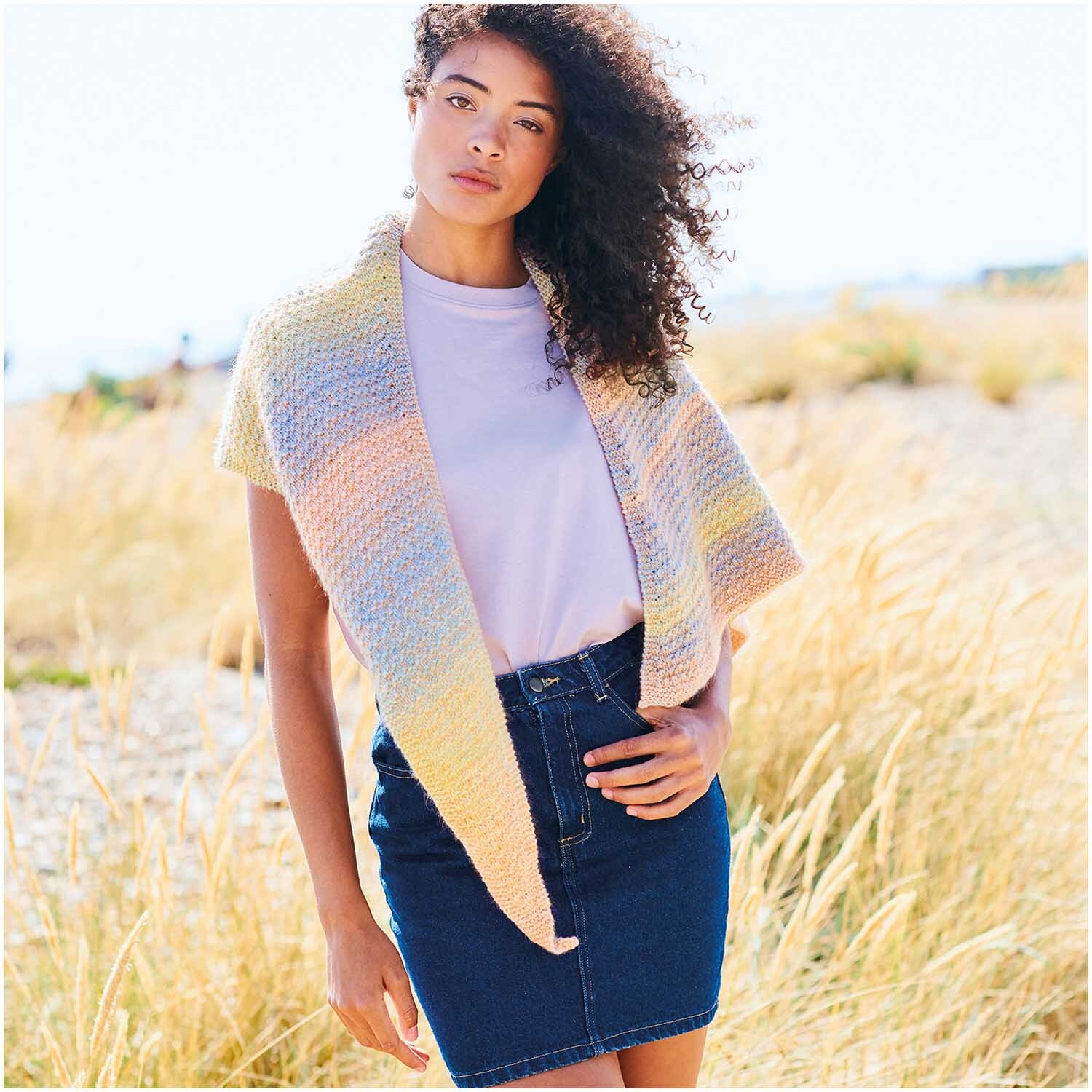 Fashion Cotton Light & Long dk: Frau trägt pastellfarbenen Schal von Rico Design, kombiniert mit weißem Shirt und Jeansrock in sonniger Landschaft.