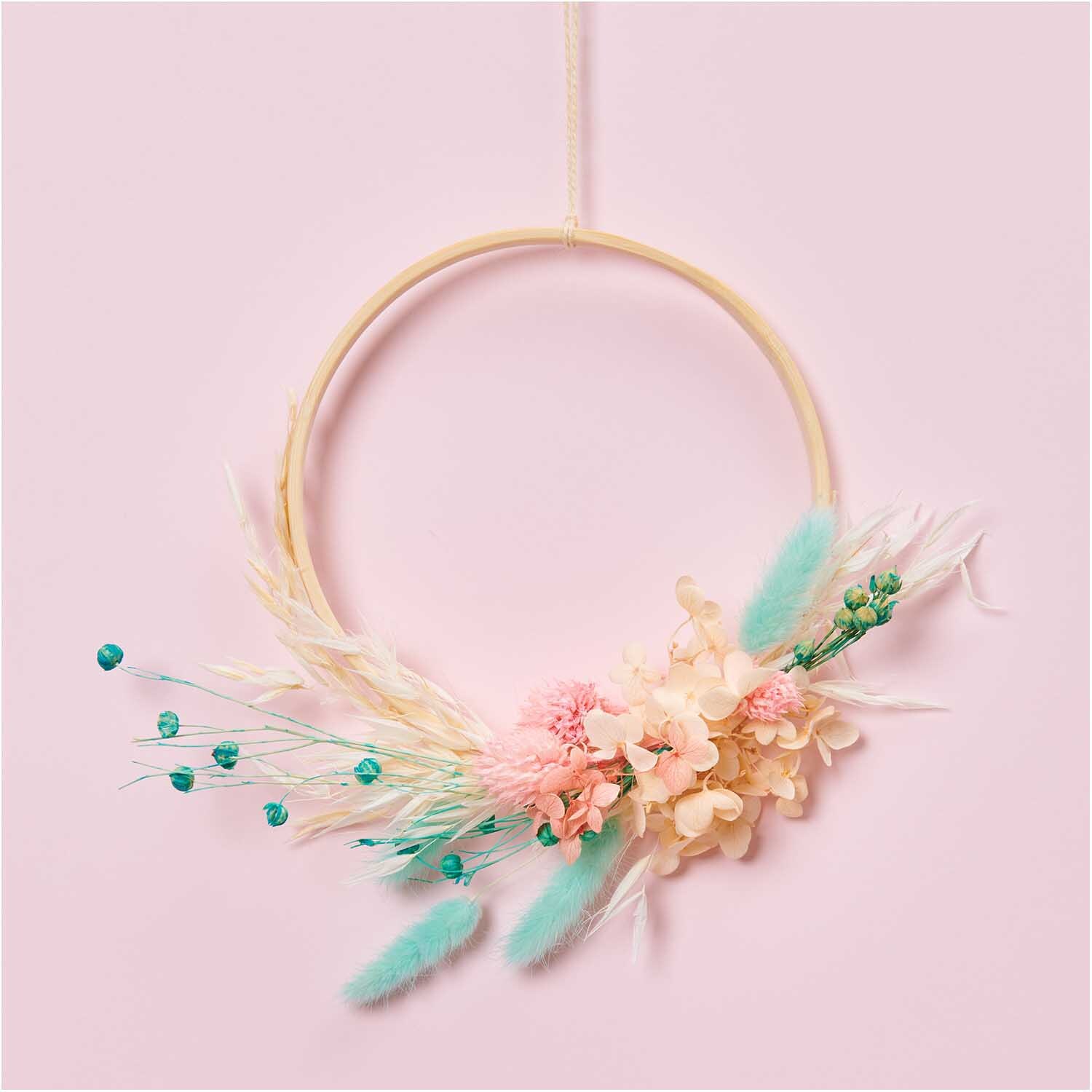 Getrockneter Flachs türkis 60-75cm 100g: Dekorativer Kranz mit türkisfarbenem Flachs und pastellfarbenen Blüten auf rosa Hintergrund. Ideal für stilvolle Raumgestaltung.