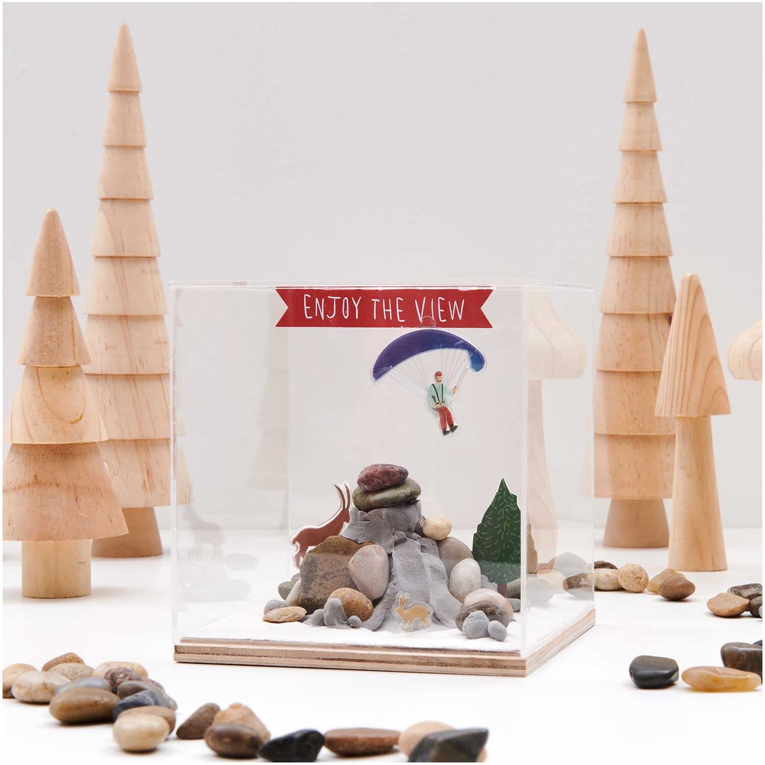 Figurico Modelliermasse 28g: Diorama mit Holzfiguren, Steinen und einem Paraglider in einer klaren Box.