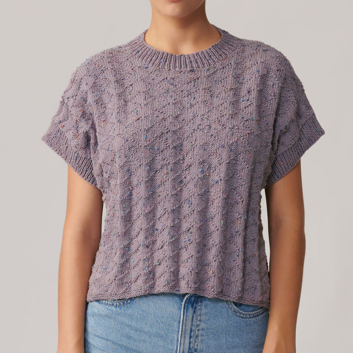 Strickanleitung Top aus Fashion Cotton Neps dk: Lila gestricktes Top mit kurzen Ärmeln und Rundhalsausschnitt, getragen von einer Person in Jeans.