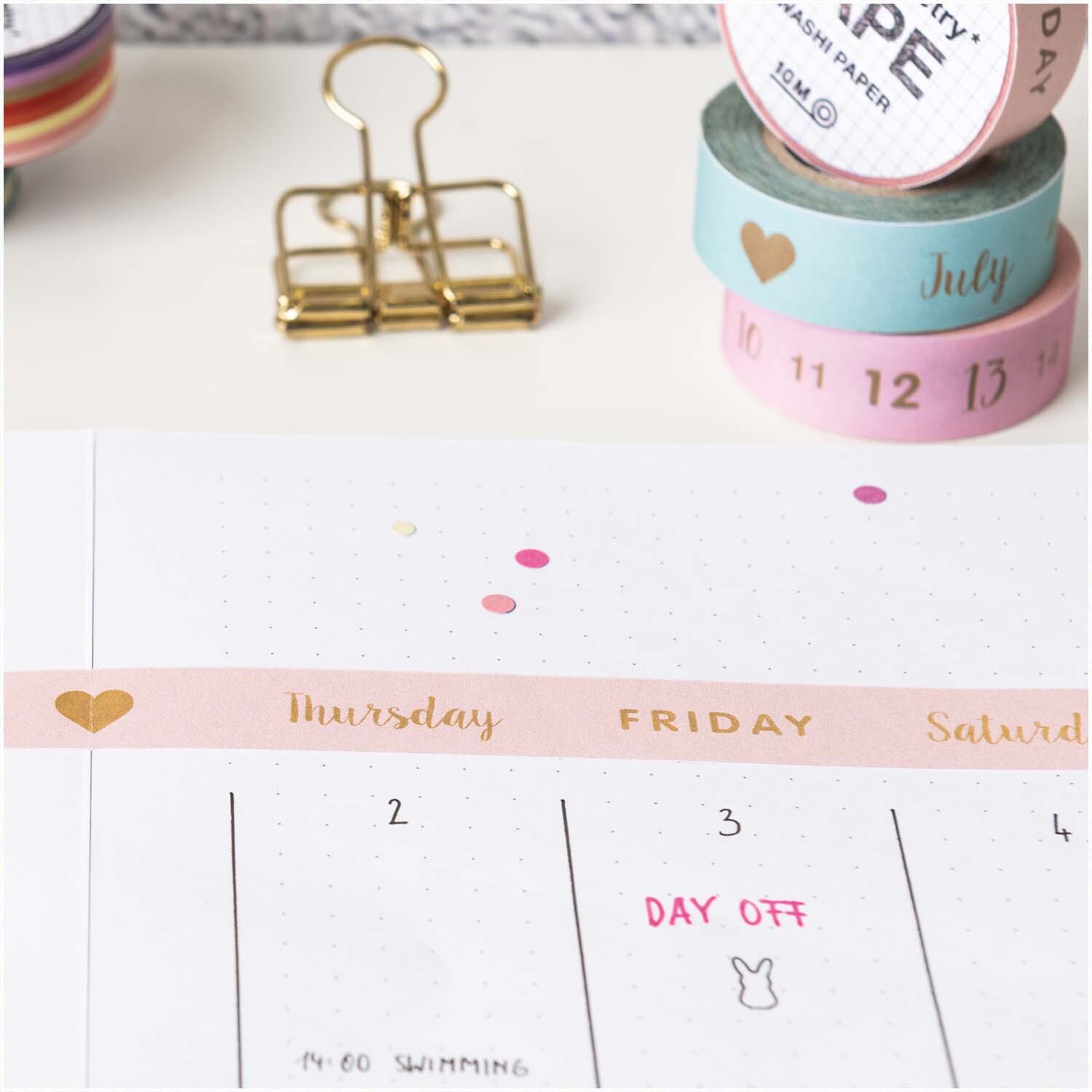 Paper Poetry Tape Zahlen 1-31 1,5cm 10m dekoriert einen Kalender mit rosa und blauen Tönen. Markenname: Rico Design.