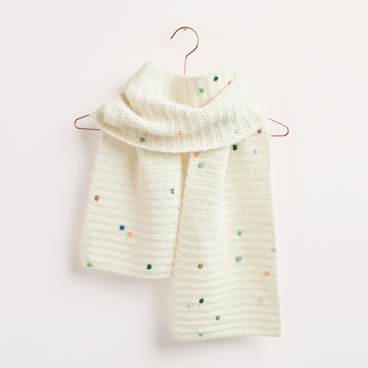 Häkelset Schal Modell 07 aus Made by Me No. 19. Ein gestrickter Schal mit bunten Punkten, präsentiert auf einem Kleiderbügel. Ideal für Herbst-Winter.