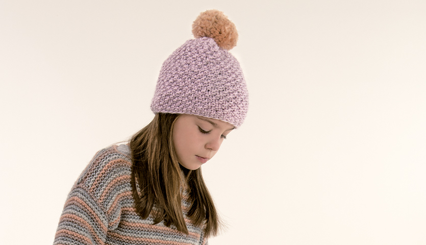 Strickanleitung Ringelpullover für Kinder: Mädchen trägt gestreiften Pullover und rosa Mütze mit Bommel.