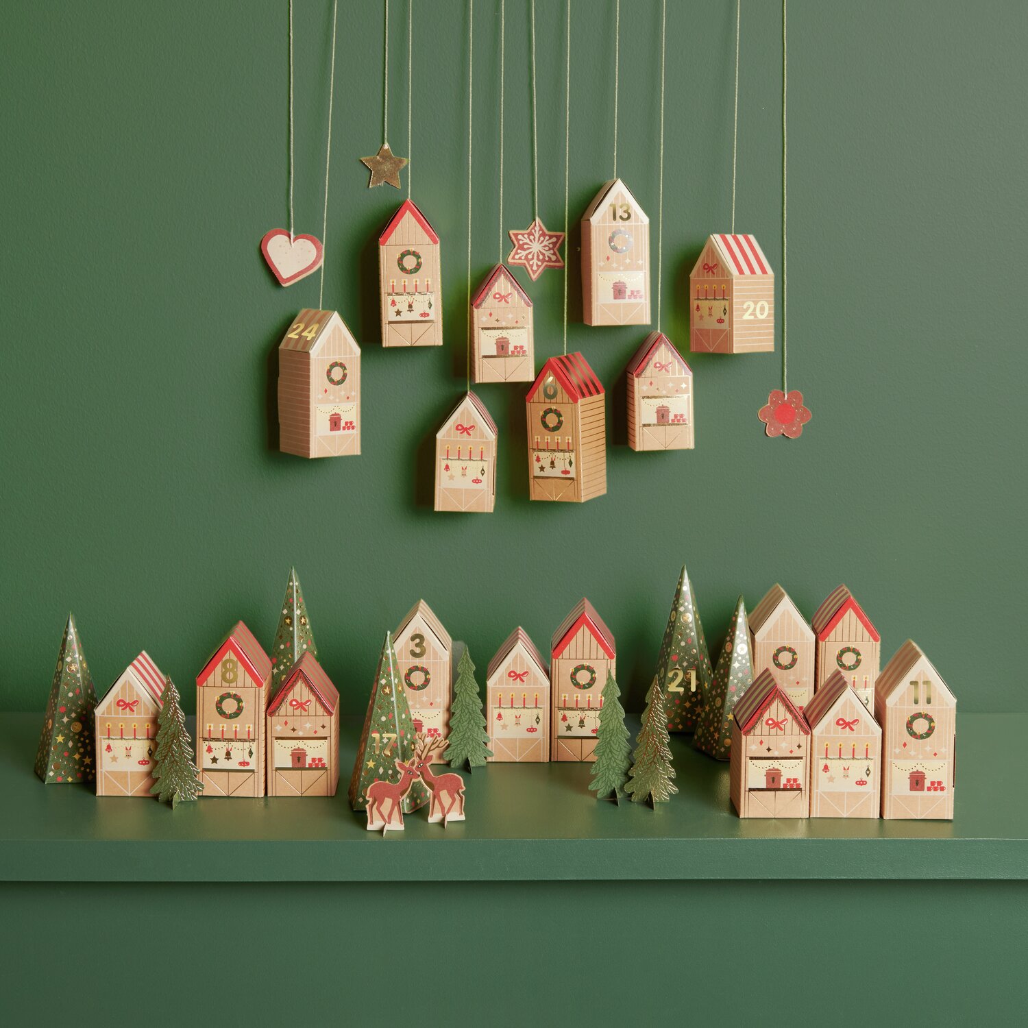 Adventskalender Bastelset mit 24 kleinen Häusern in Rot und Beige, dekoriert mit Tannenbäumen.