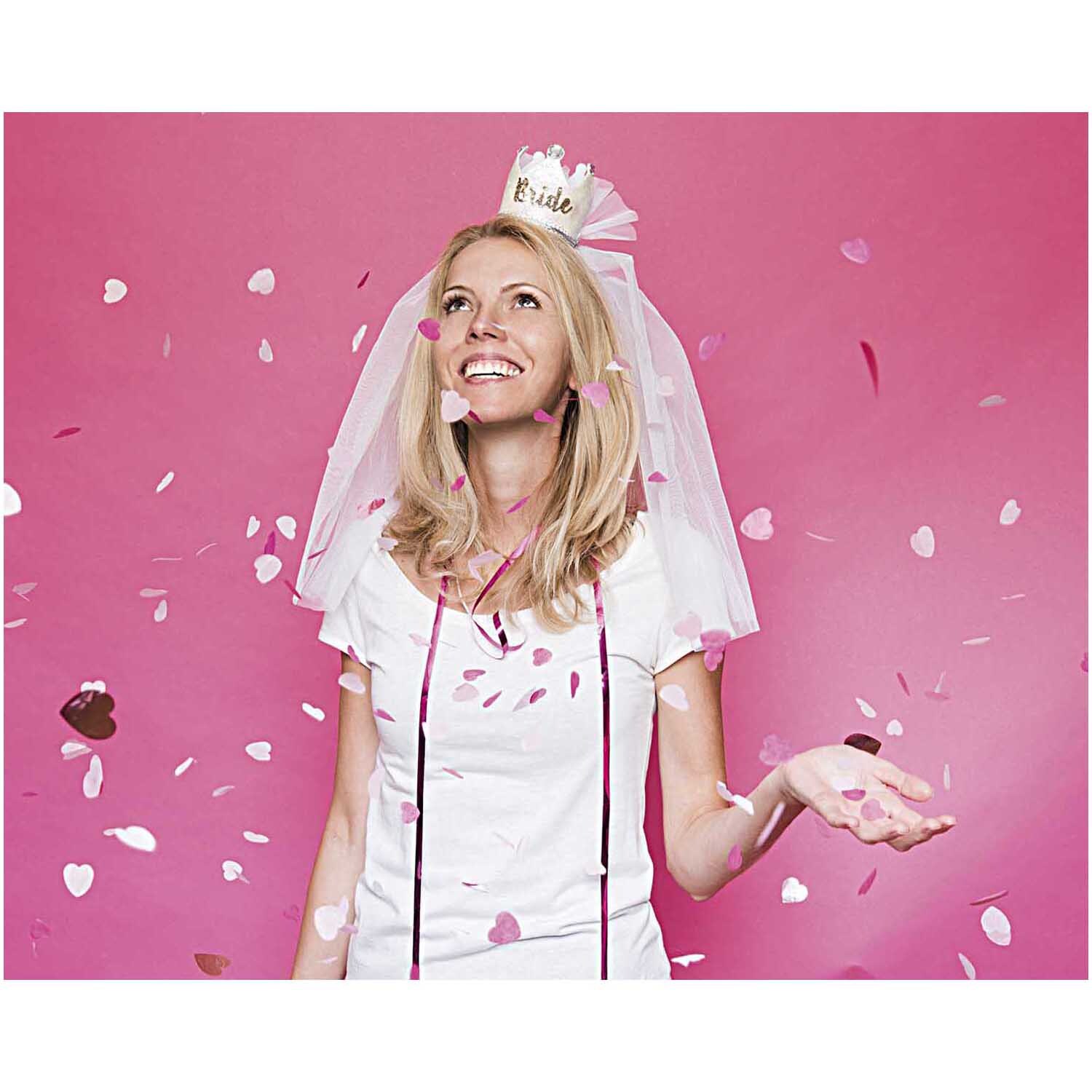 Partykrone Bride 8,5cm auf weißem Schleier, Frau lächelnd vor pinkem Hintergrund mit Konfetti.
