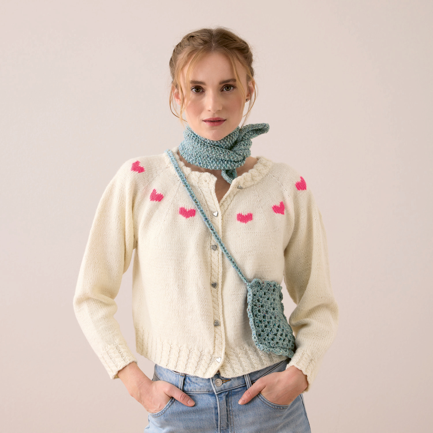 Strickset Cardigan Modell 17 aus Trachtenbuch I mog di: Cremefarbener Cardigan mit neon-pinken Herzen, kombiniert mit hellblauer Tasche und Schal.