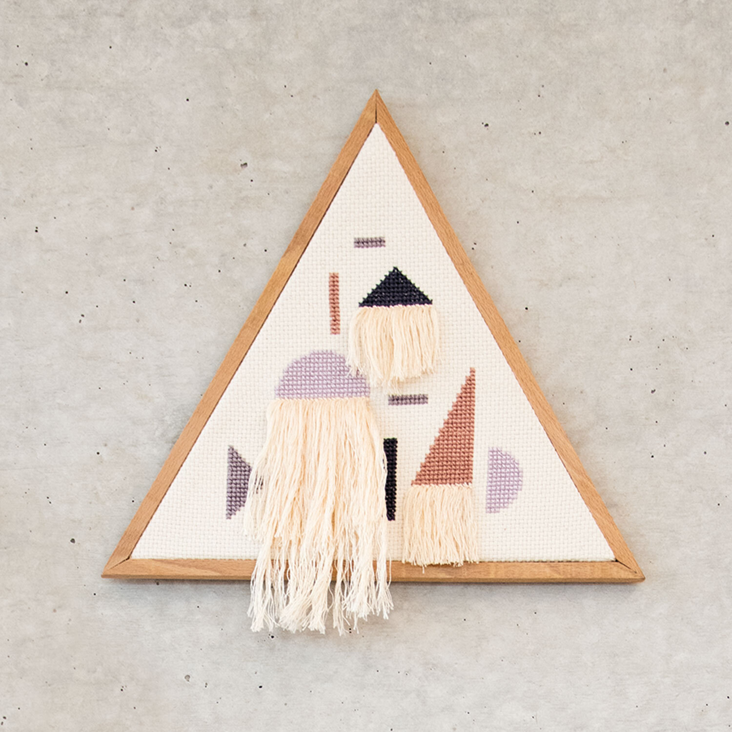 Stickanleitung DIY Wanddeko im Dreiecksrahmen mit geometrischen Mustern und Fransen auf hellem Hintergrund.