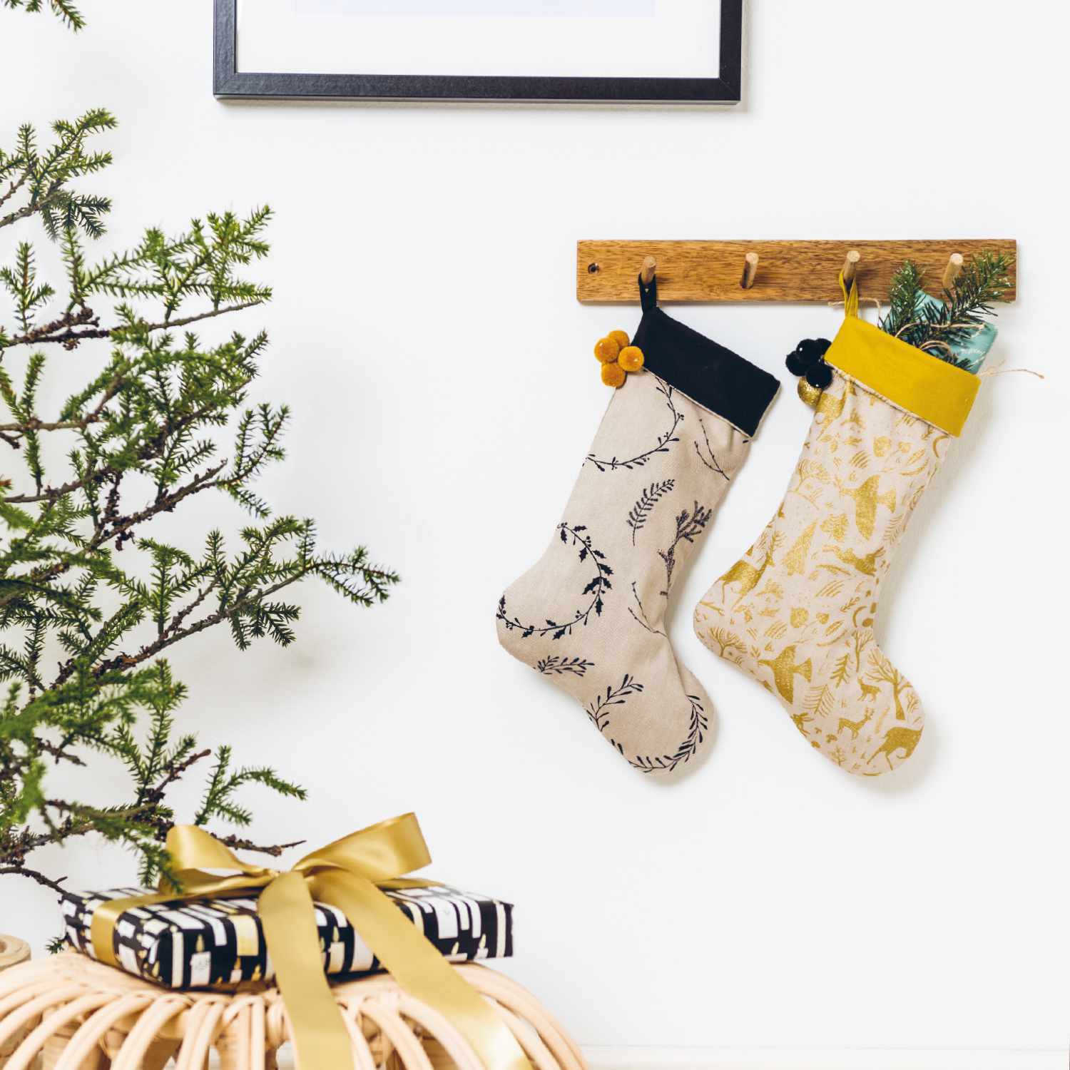 Nähanleitung Nikolaus-Stiefel: Zwei dekorative Stiefel an einer Holzleiste, einer mit Pflanzen gefüllt, daneben ein Geschenk mit goldener Schleife.