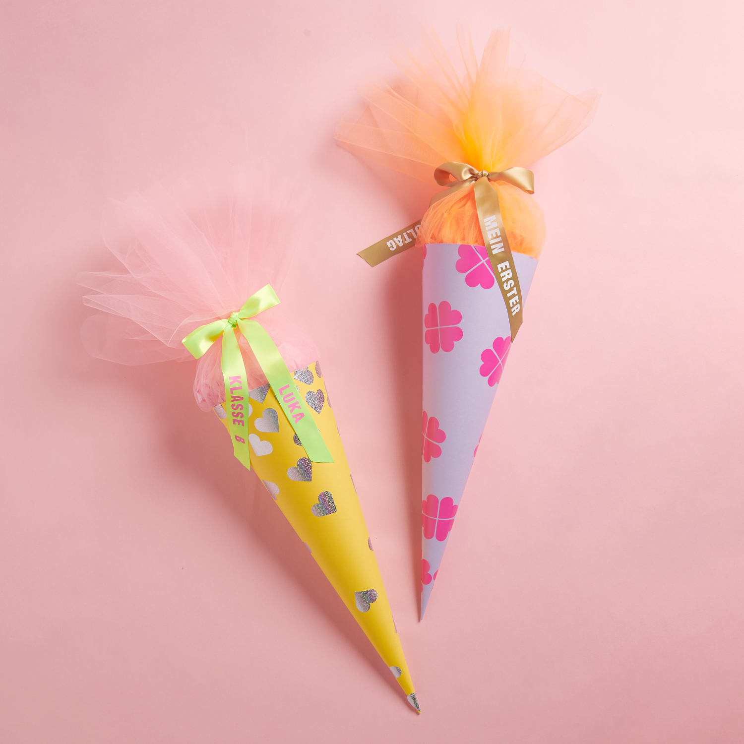 Bastelanleitung Schultüte mit Stickern verzieren: Zwei bunte Schultüten mit Schleifen und Stickern auf rosa Hintergrund.
