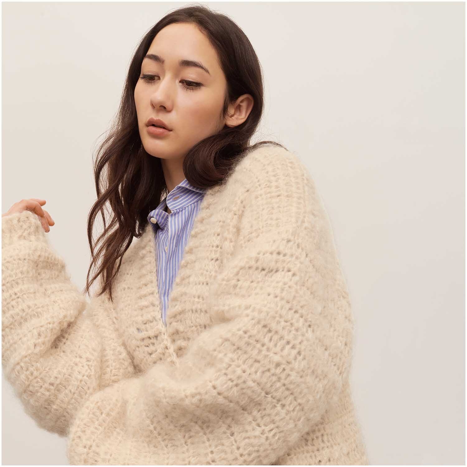 Häkelset Cardigan Modell 03: Frau trägt einen beigen, grob gestrickten Cardigan über einem blauen Hemd.