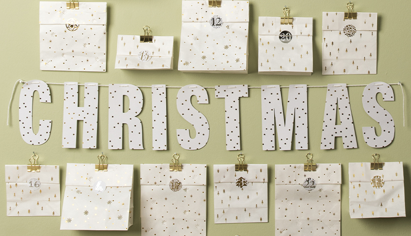 Bastelanleitung Adventskalender aus Lichtertüten: Weiße Tüten mit goldenen Clips und Weihnachtsmotiv.