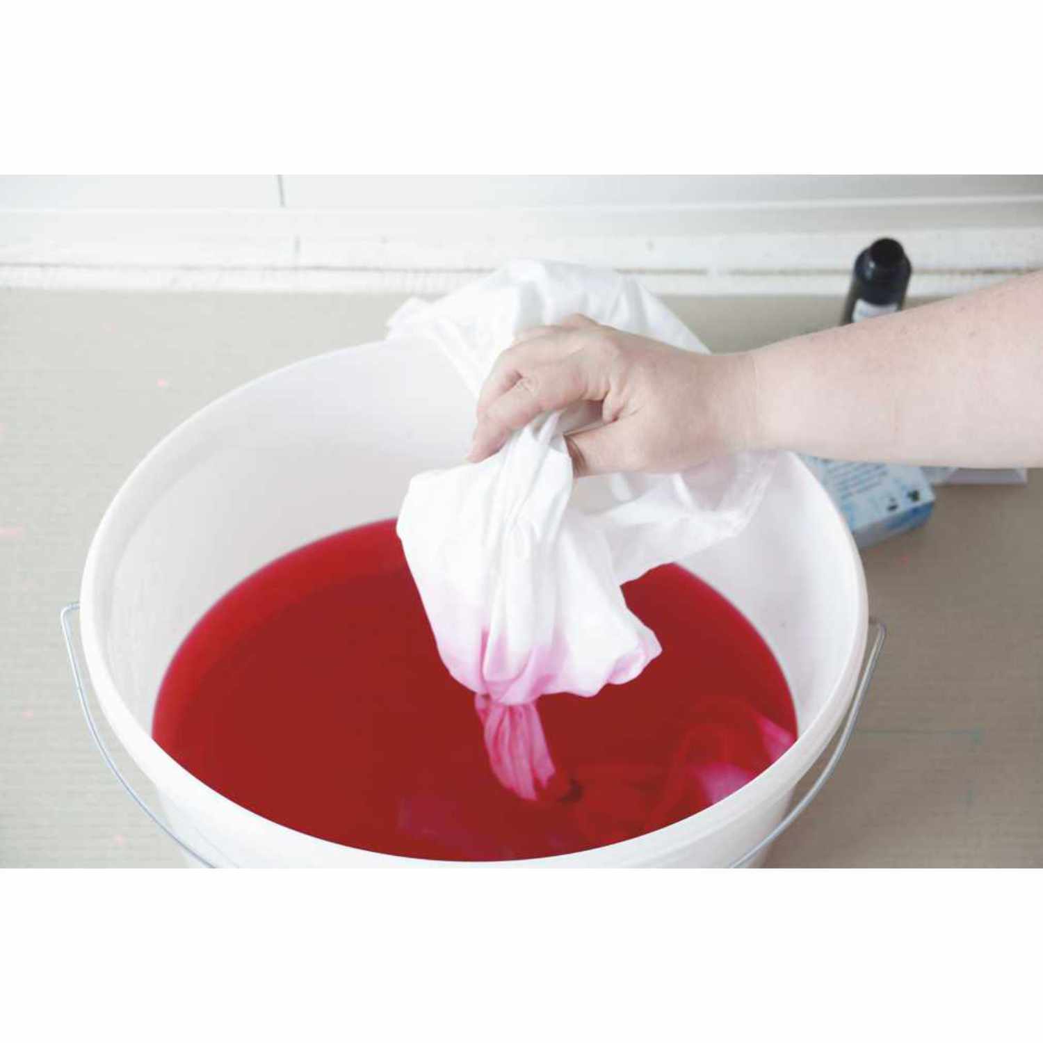 Javana Batik-Textilfarbe: Eine Hand taucht weißen Stoff in rote Farbe in einem Eimer. Ideal für kreative Textilgestaltung.