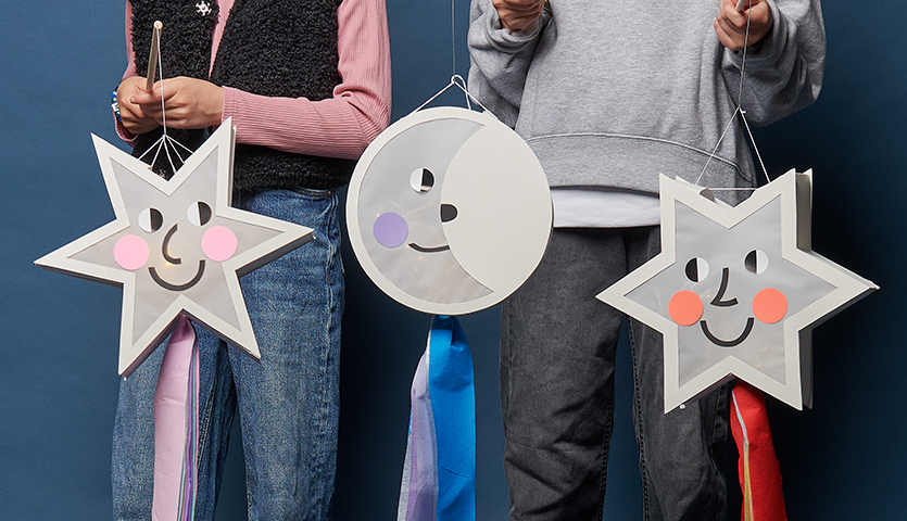 Bastelanleitung Laterne Sterne und Mond: Zwei Kinder halten kreative Laternen in Stern- und Mondform mit fröhlichen Gesichtern und bunten Bändern.