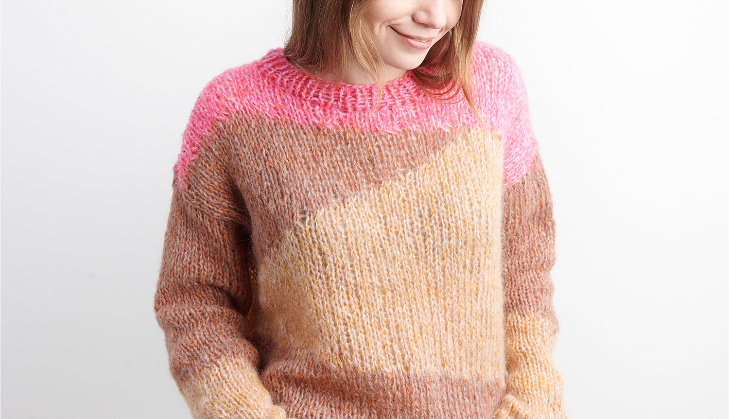 Strickanleitung Pullover mit geometrischem Muster: Frau trägt Pullover in Braun- und Rosatönen.