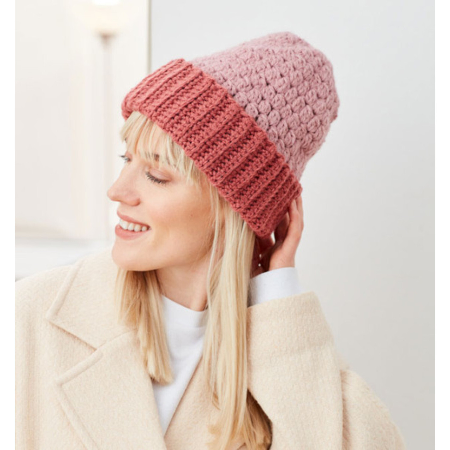 1x1 Häkeln - Grundwissen, Modelle & Inspirationen: Frau mit rosa gehäkelter Mütze, lächelnd.