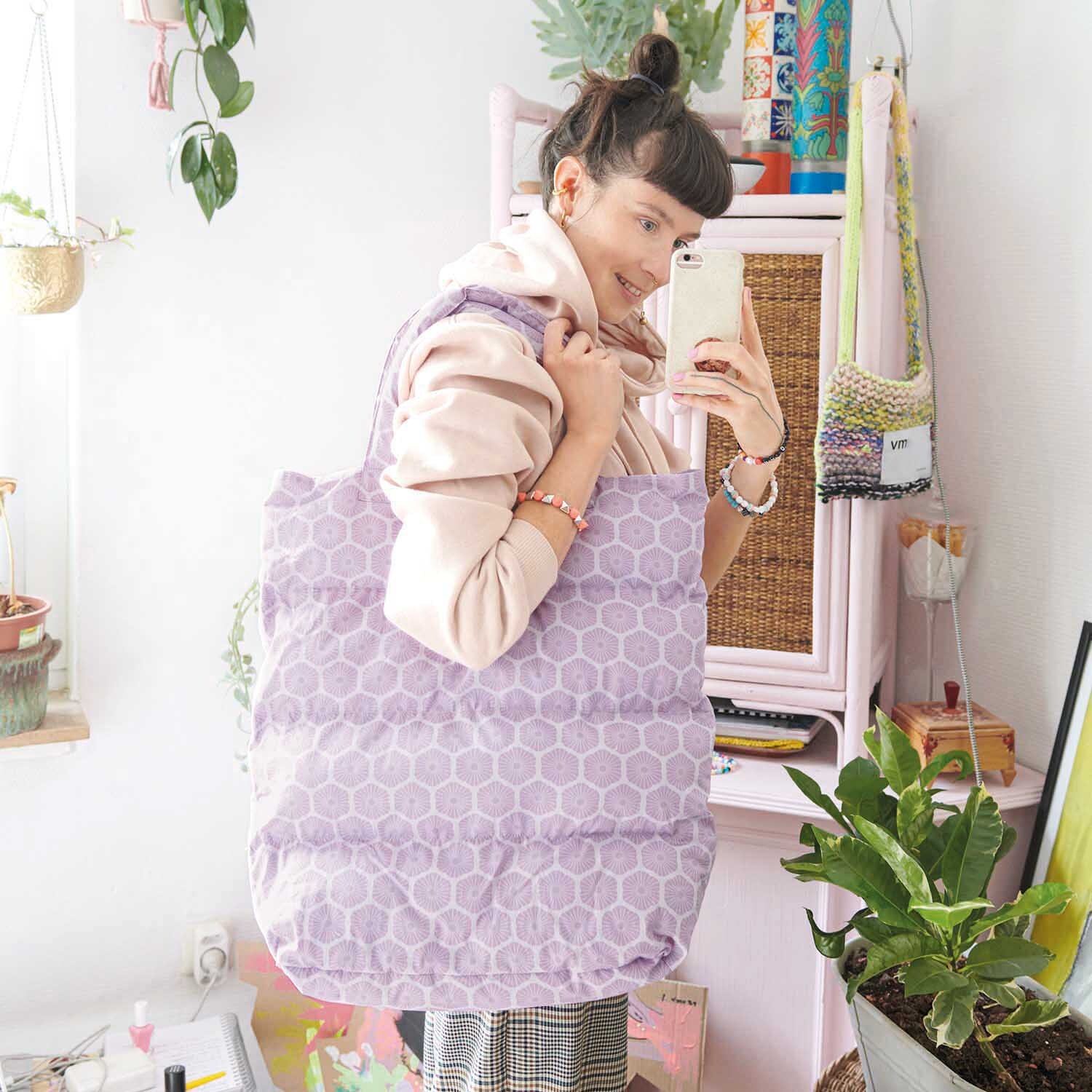 Nähanleitung Puffer Bag: Frau mit großer, lila gepolsterter Tasche in einem hellen Raum mit Pflanzen.