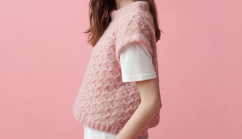 Strickanleitung Pullunder aus Fashion Skinny Alpaca aran: Rosa Pullunder über weißem T-Shirt vor rosa Hintergrund.