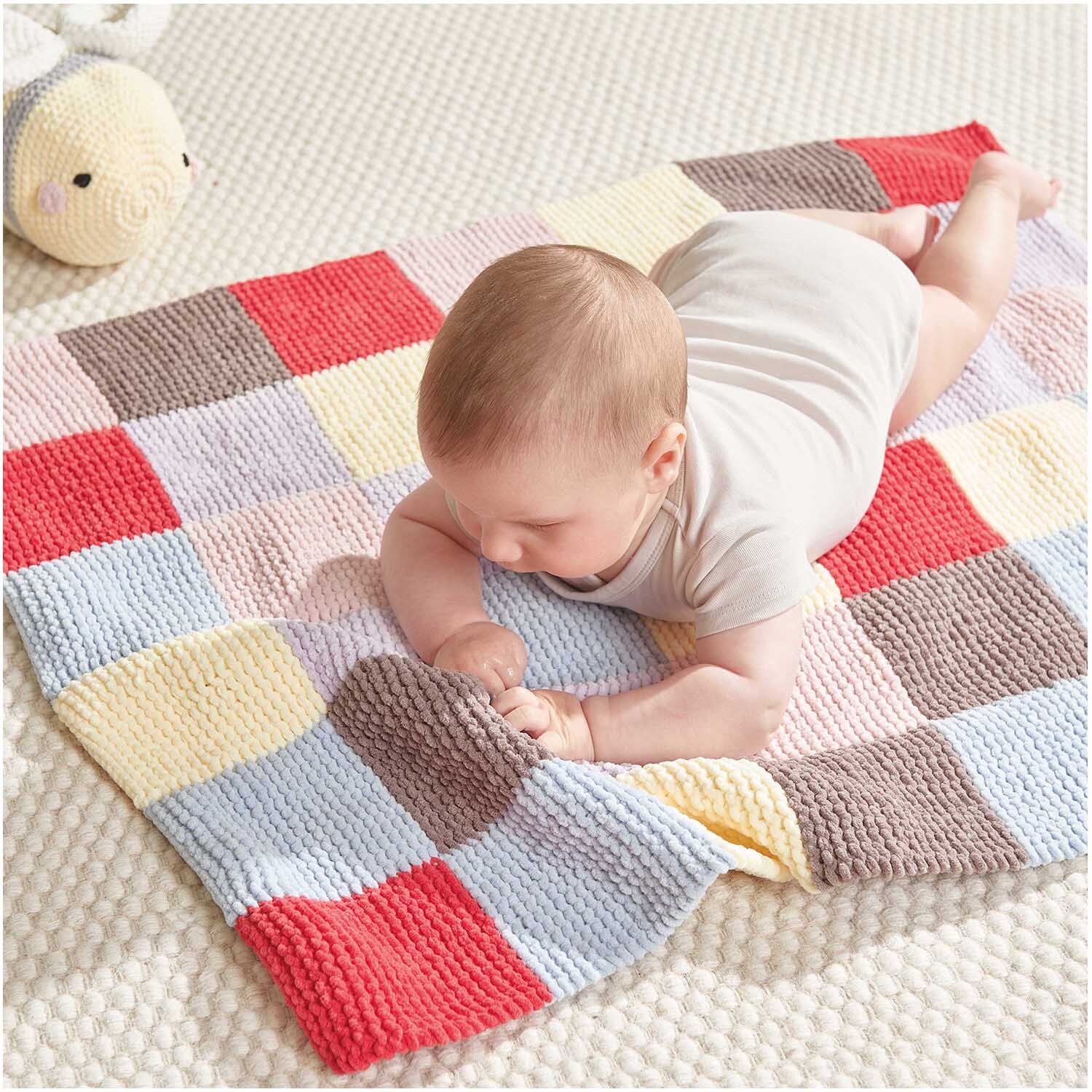 Häkelset Biene Modell 10 aus Baby Chenillove: Ein Baby liegt auf einer bunten, gehäkelten Decke mit quadratischem Muster.