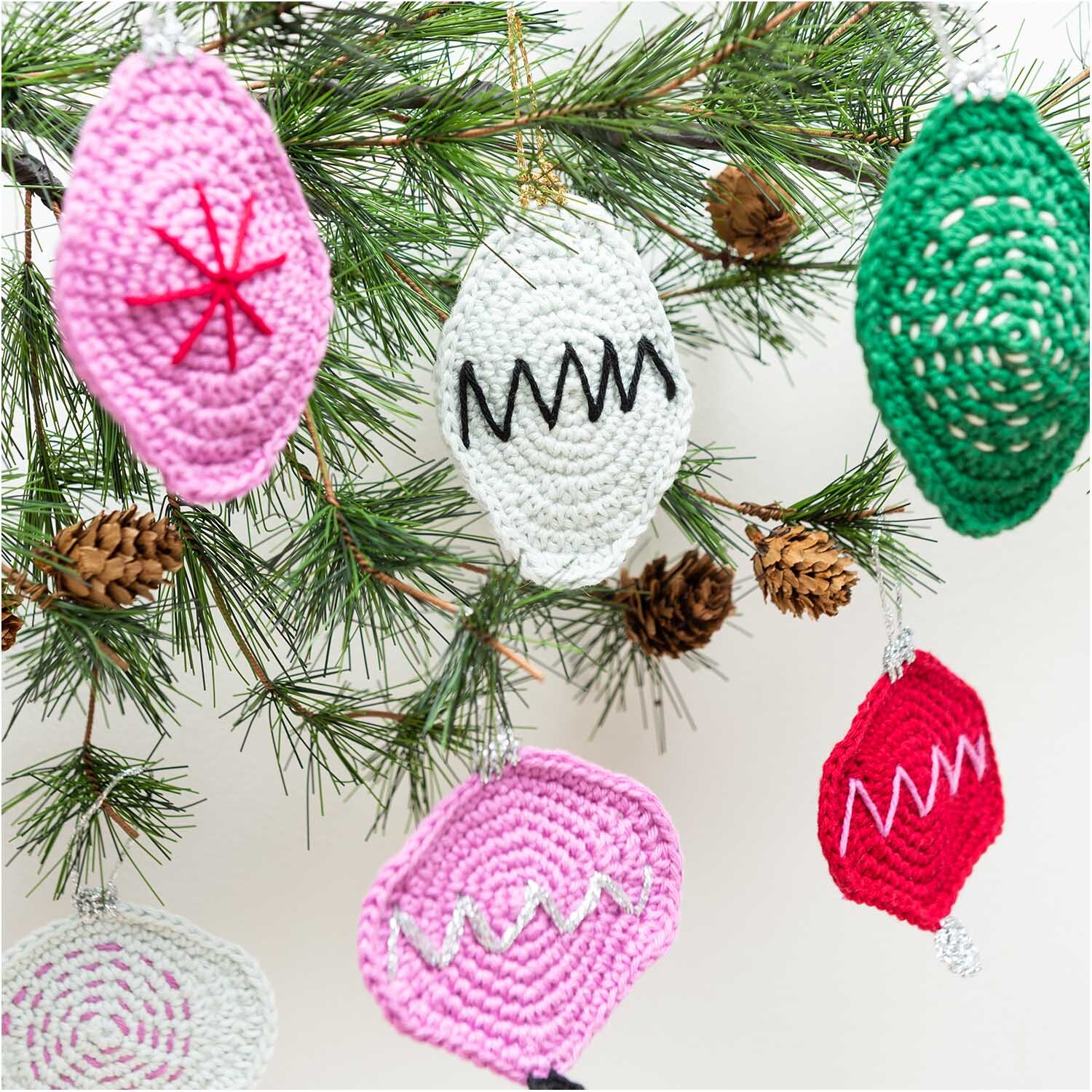 Creative Ricorumi dk: Gehäkelte Weihnachtsornamente in verschiedenen Farben an einem Tannenzweig.