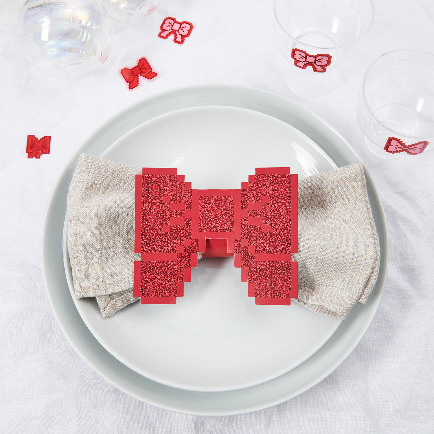 Paper Poetry Serviettenringe Schleifen Pixel in Rot auf einem gedeckten Tisch mit weißem Geschirr und Leinenserviette, 6er-Set von Rico Design.
