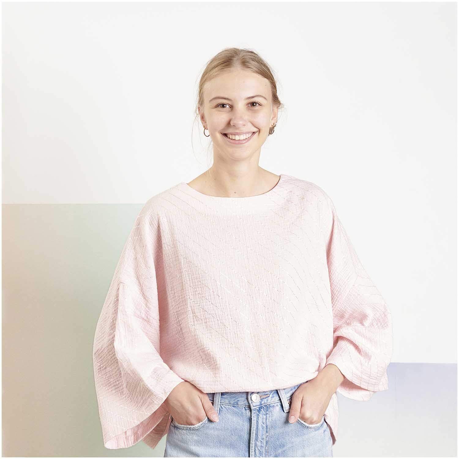 Stoffabschnitt Krinkelmusselin Streifen Rosa: Frau in rosa Oberteil aus Krinkelmusselin von Rico Design, lächelnd, vor hellem Hintergrund.