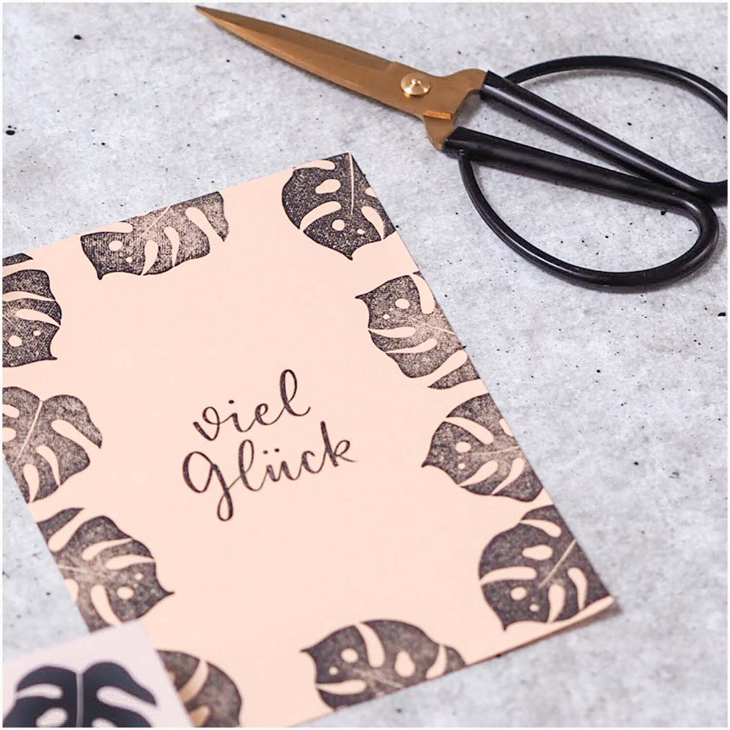 Stempel viel Glück nude 45x45mm von May&Berry auf rosa Papier mit Monstera-Muster und Schere.
