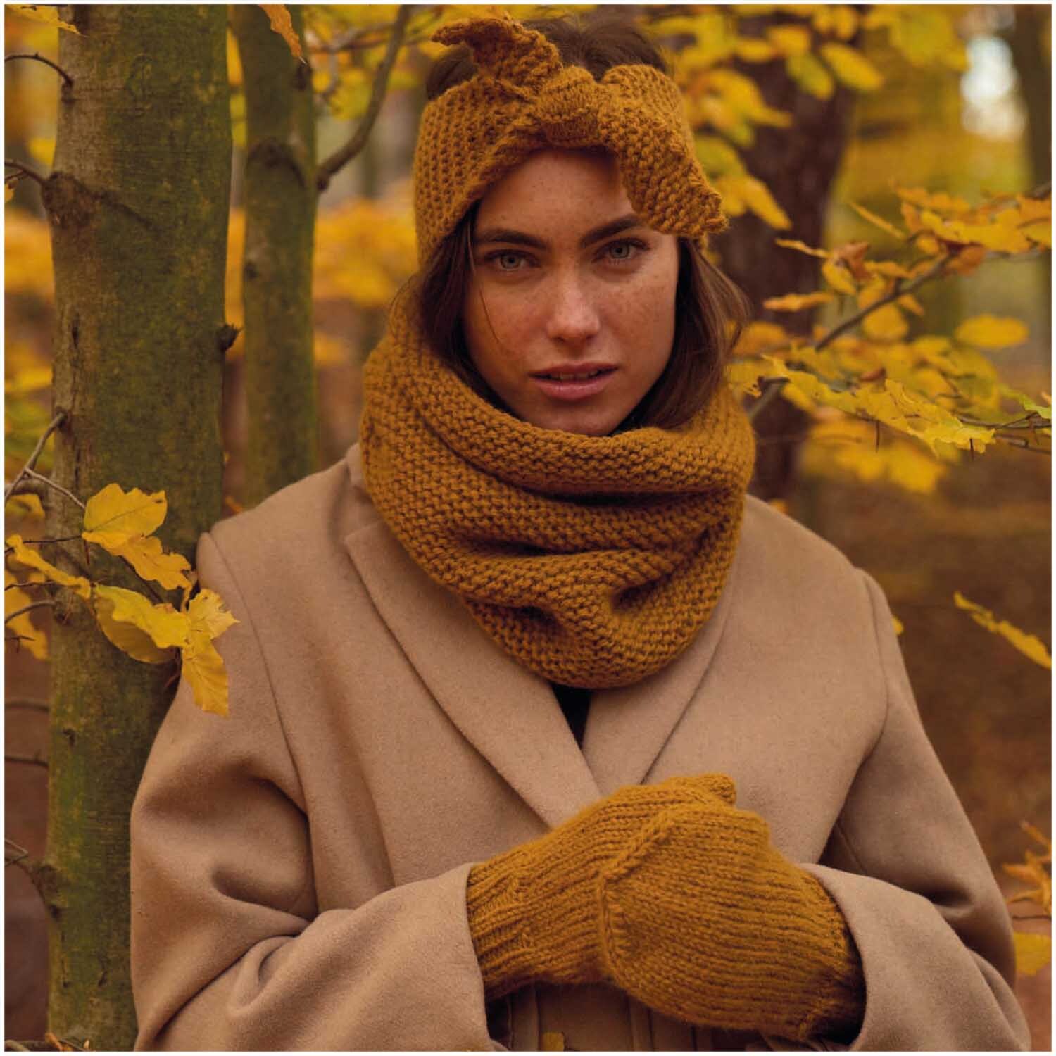Essentials Alpaca Twist Chunky: Frau im Wald mit karamellfarbenem Schal, Stirnband und Handschuhen aus Rico Design Wolle.
