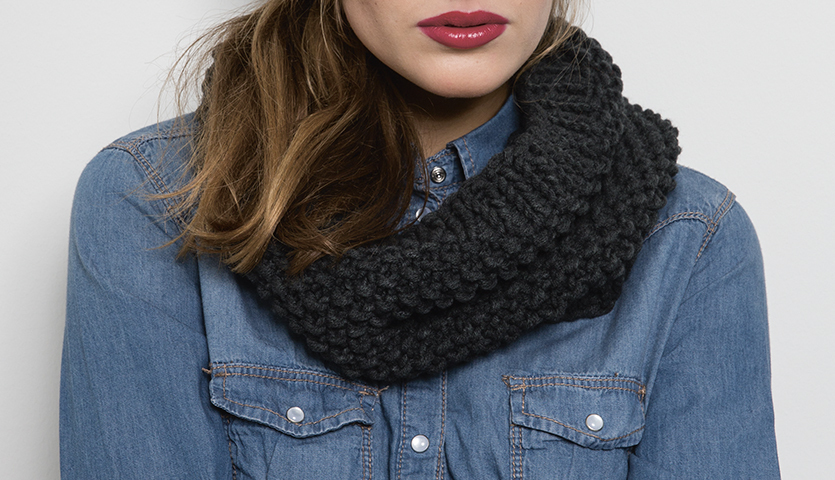 Strickanleitung Stirnband und Loop aus Polar: Frau trägt einen dunkelgrauen Loop-Schal über einem blauen Jeanshemd.