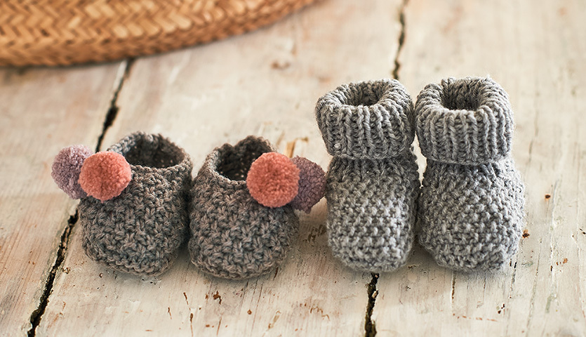 Strickanleitung Babysocken aus Rico Baby Classic dk: Zwei Paar graue, handgestrickte Babysocken auf einem Holztisch.