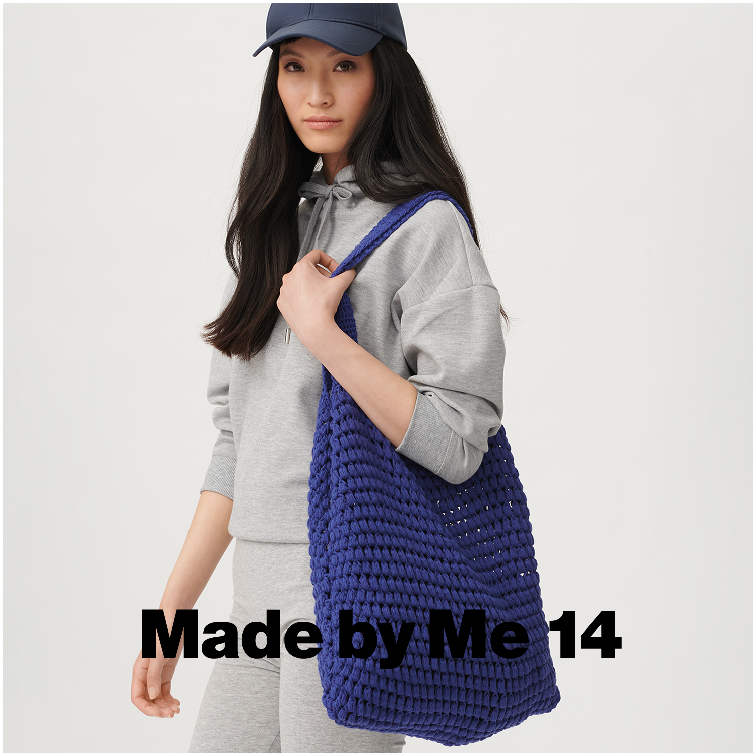 Creative Cotton aran: Frau in grauem Hoodie und Mütze trägt eine große, gestrickte Tasche in Veilchen.