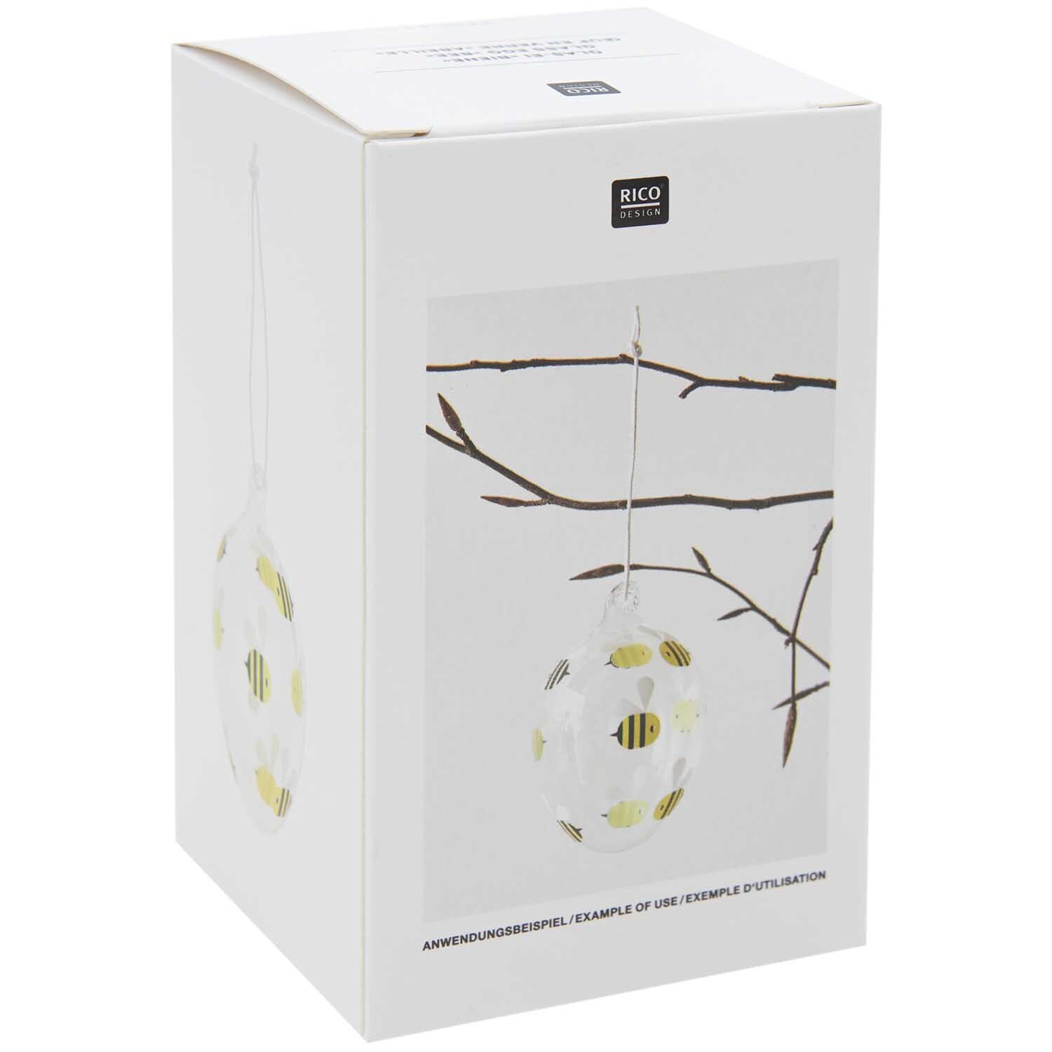 Glas Ei Biene Ø 6cm von Rico Design, dekoriert mit Bienenmotiv, hängt an einem Ast.
