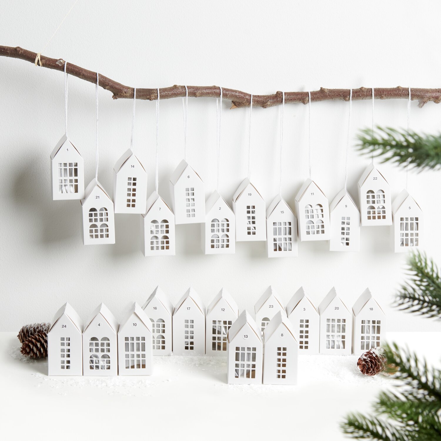 Adventskalender Papphäuser 24 Stück: Weiße Häuschen von Rico Design, dekorativ an Ast hängend.