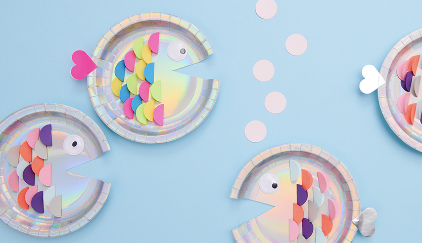Bastelanleitung Fische aus Papptellern: Bunte Pappteller-Fische auf blauem Hintergrund, kreativ gestaltet.