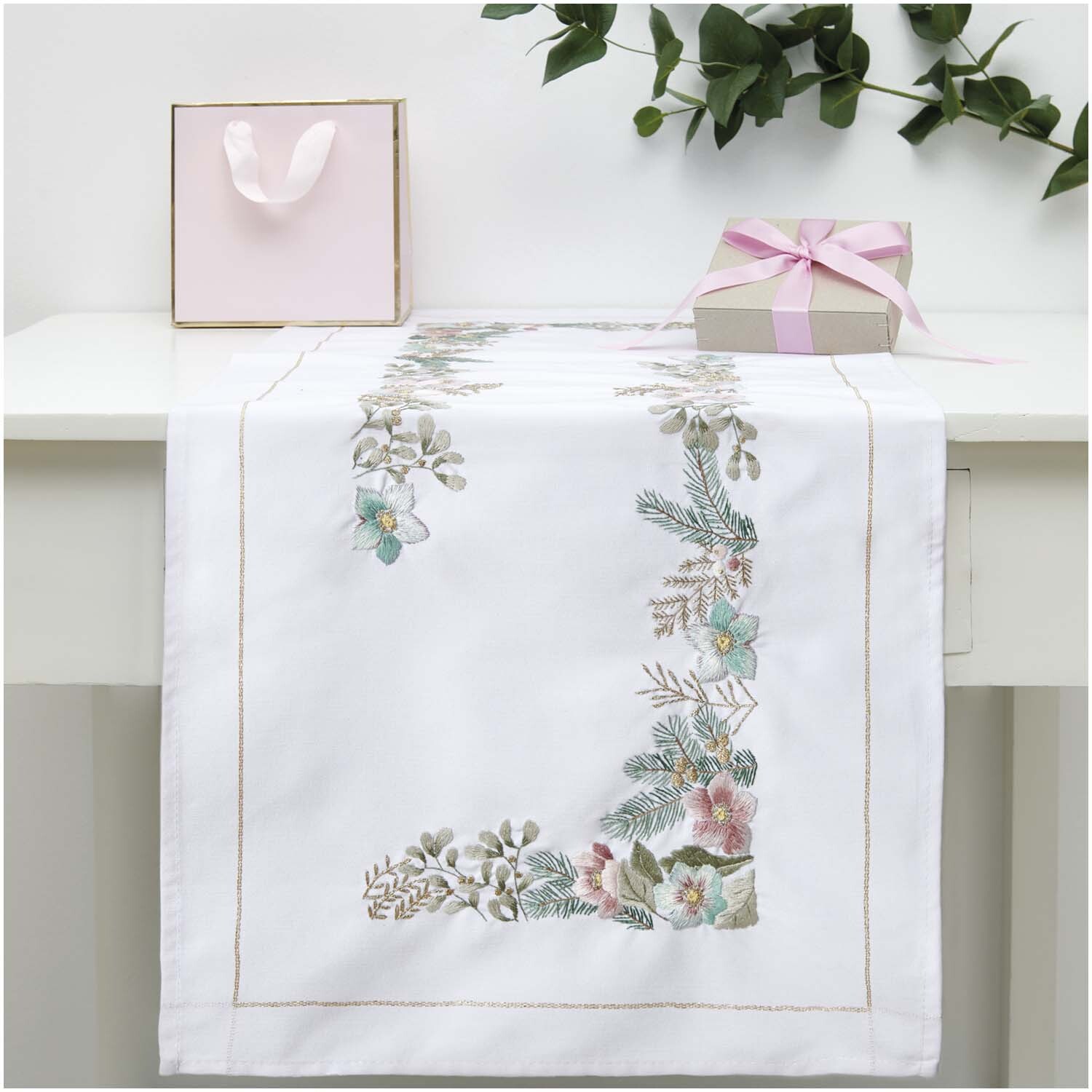 Stickpackung Läufer Christrosen von Rico Design auf weißem Tisch mit floralen Stickereien und Geschenkbox.