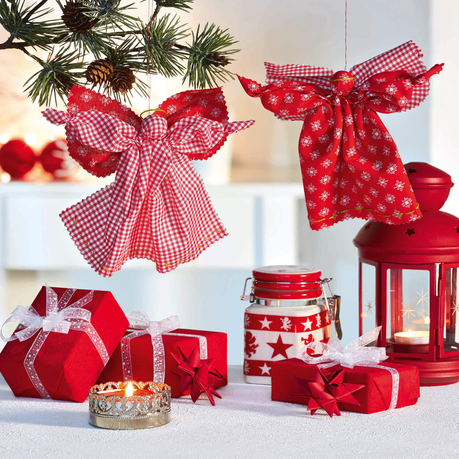 Nähanleitung Stoffengel: Zwei rote Stoffengel hängen an einem Ast, umgeben von weihnachtlichen Dekorationen.