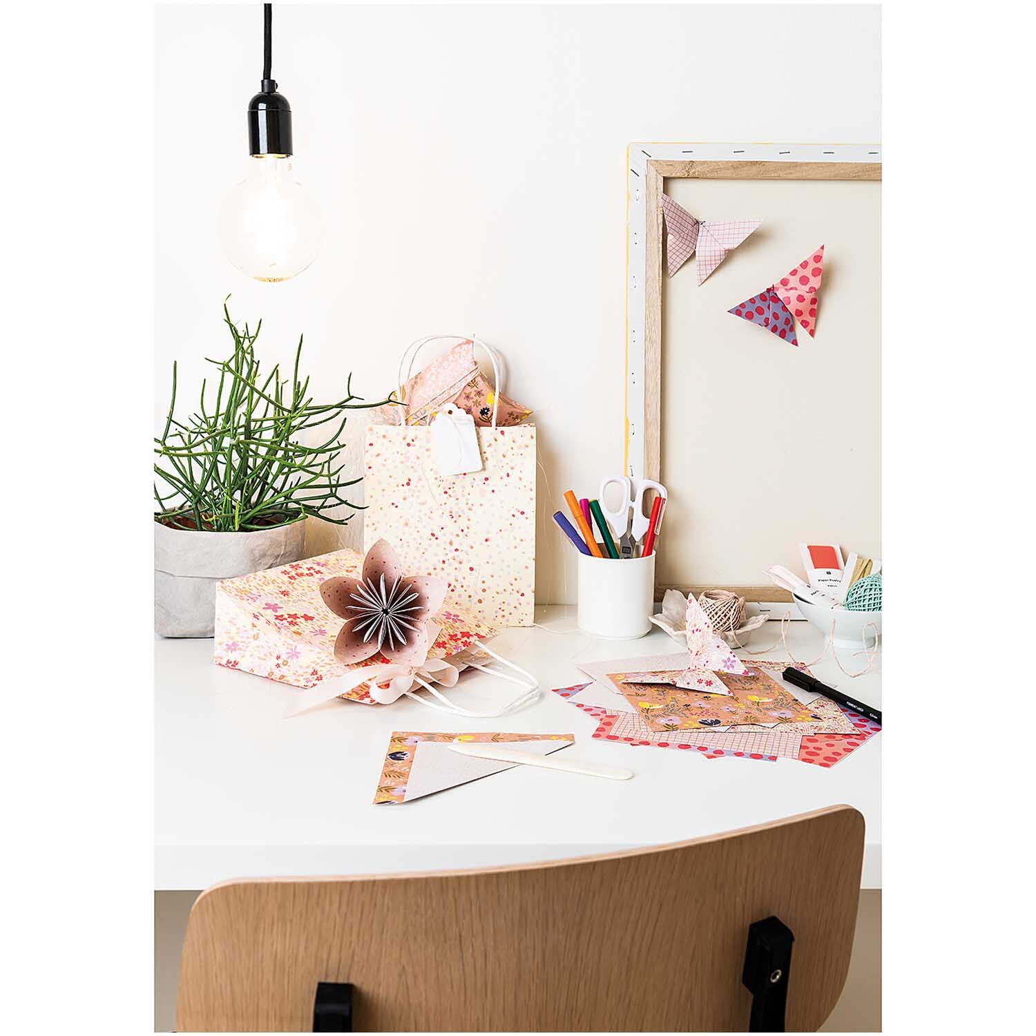 Paper Poetry Geschenkschachteln auf einem Schreibtisch mit Bastelmaterialien und Pflanzen, ideal für kreative Geschenkverpackungen.