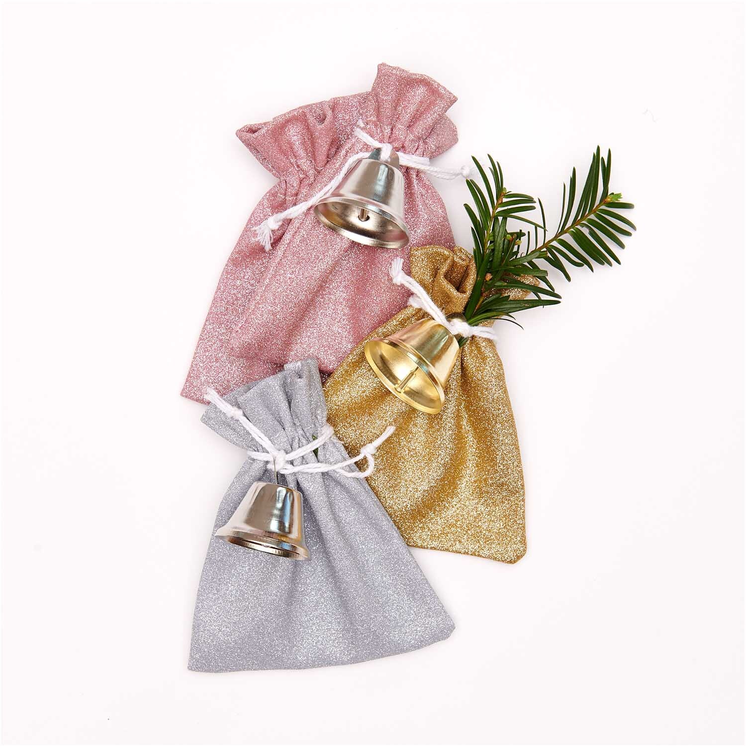 Metallglöckchen silberfarbig von Rico Design auf glitzernden Beuteln in Rosa, Gold und Silber arrangiert.