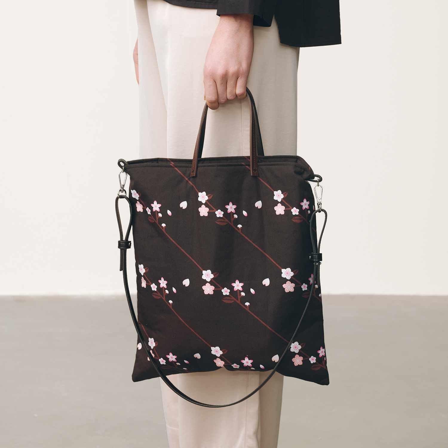 Nähanleitung Tasche mit floralem Print: Eine elegante, schwarze Tasche mit Blumenmuster, getragen von einer Person in heller Kleidung.