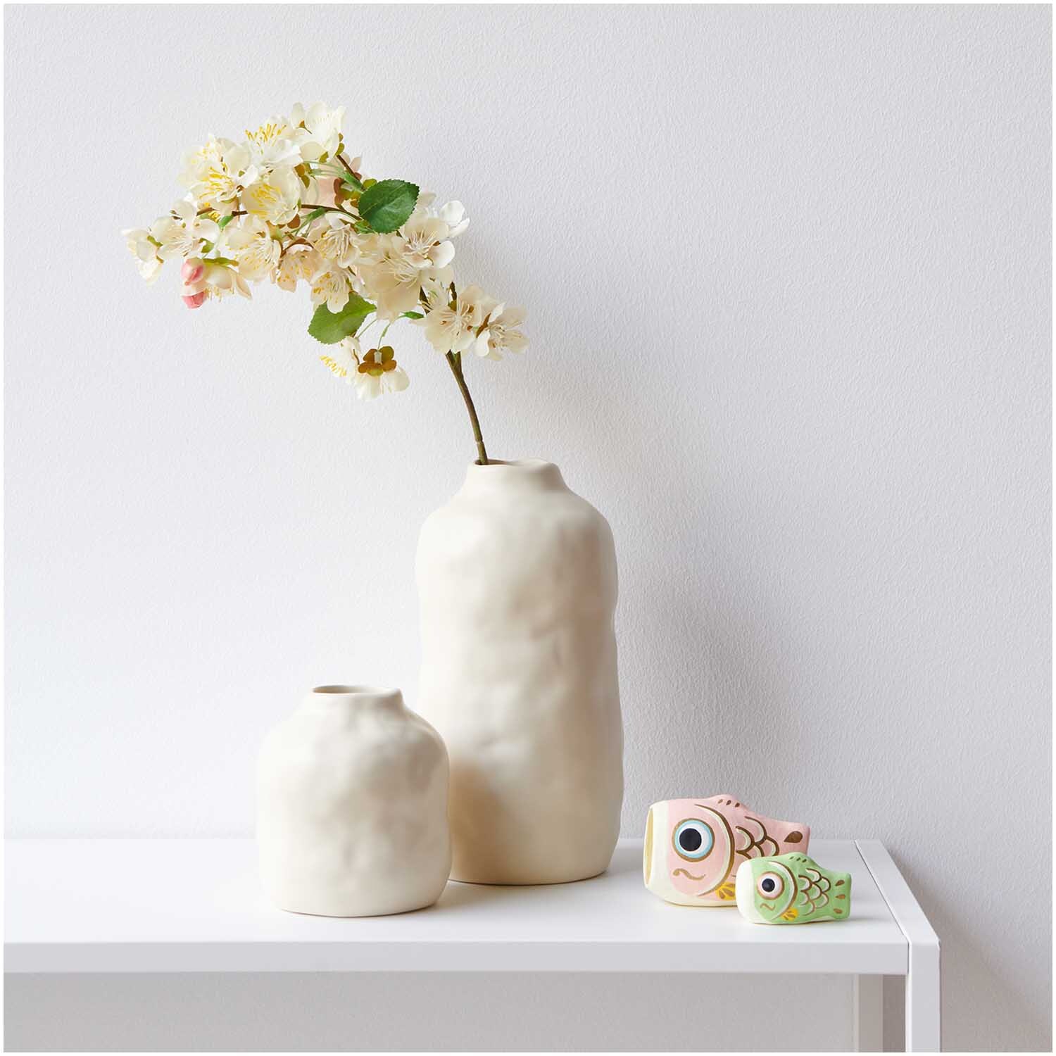 Kirschblütenzweig weiß 57cm in einer eleganten Vase von Rico Design auf einem weißen Tisch.