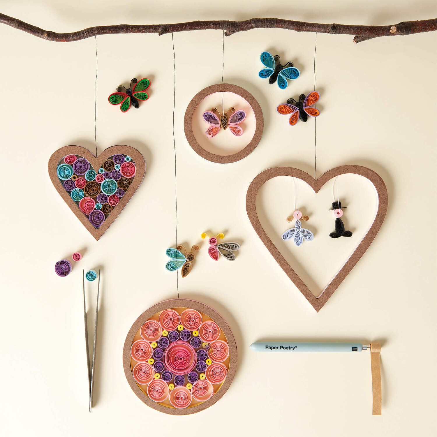Bastelanleitung Quilling: Bunte Quilling-Dekorationen in Herz- und Kreisform mit Schmetterlingen an einem Ast hängend.