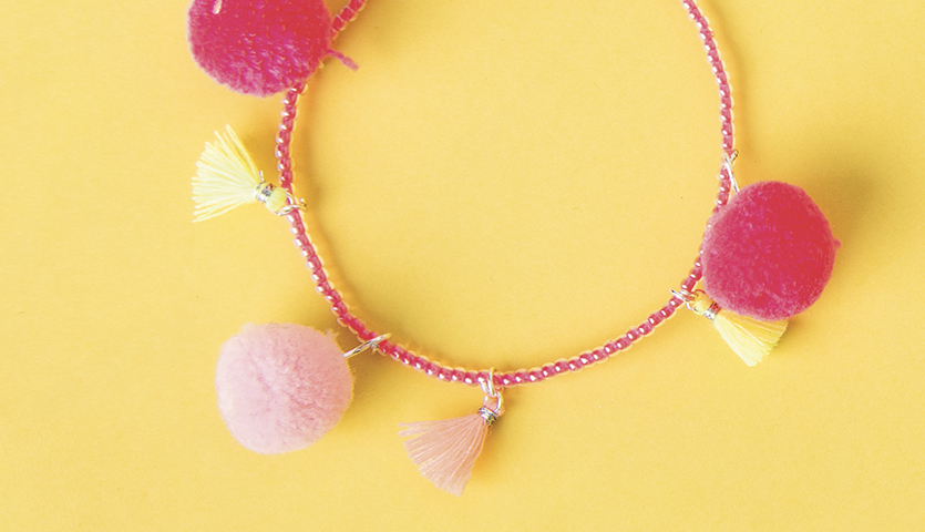 Bastelanleitung Perlenarmband mit Quasten und Pompons in Rosa und Gelb auf gelbem Hintergrund.