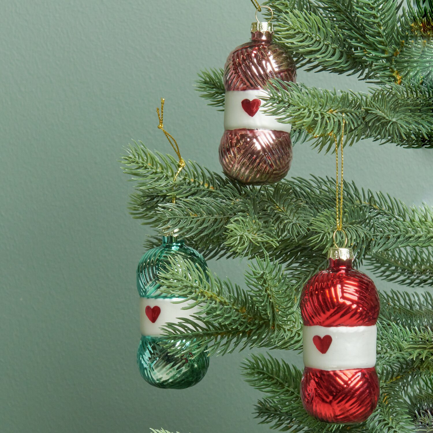 Glaskugel Wollknäuel von Rico Design in Altrosa, Grün und Rot als Christbaumschmuck an einem Tannenbaum.